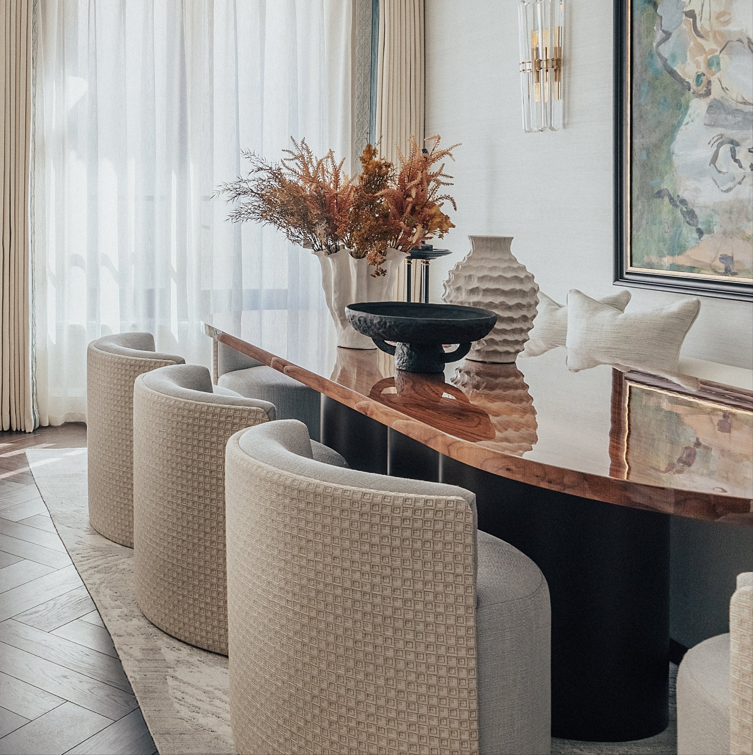 Elegant dining table with a wave-base design, featuring a curved, black sculptural base, topped with a light-colored, smooth surface.Surrounded by modern, upholstered chairs in a well-decorated dining room.