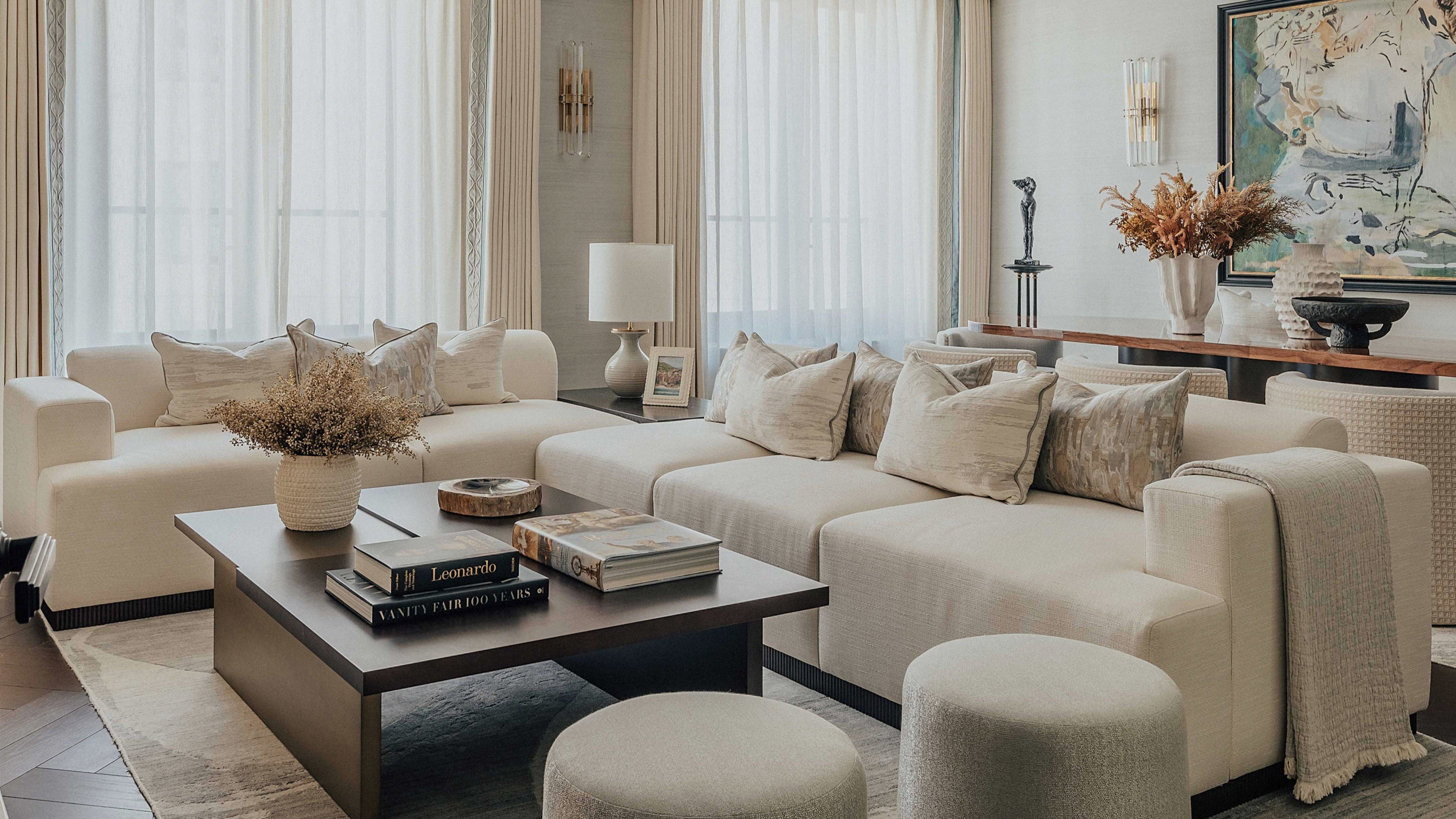 A contemporary living room at The OWO featuring a beige corner sofa with fluted wooden base, paired with a wooden coffee table and floor-length curtains.