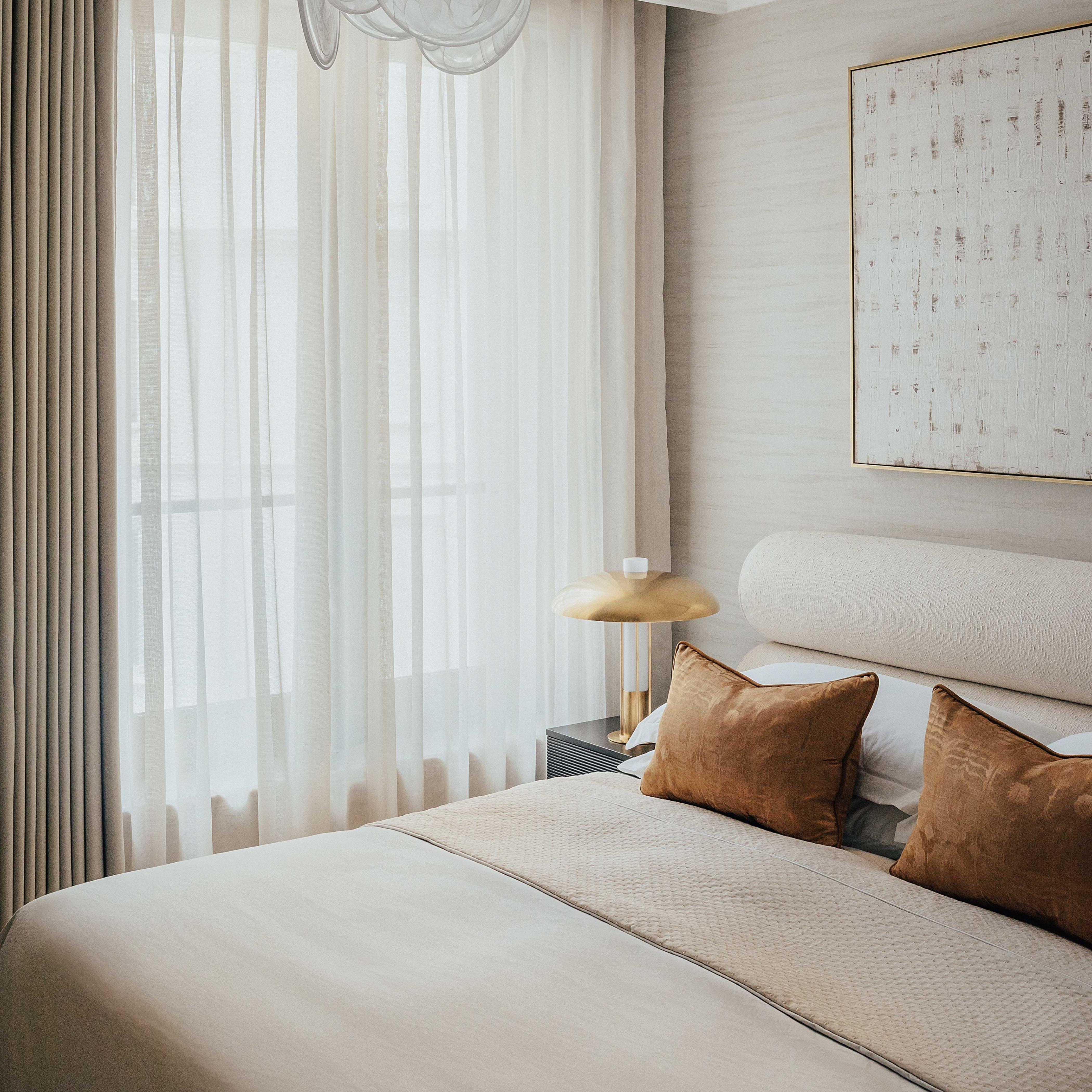 A ottoman bed with beige linen bouclé upholstery, featured in a serene bedroom setting with white curtains and brown accent pillows. The OWO